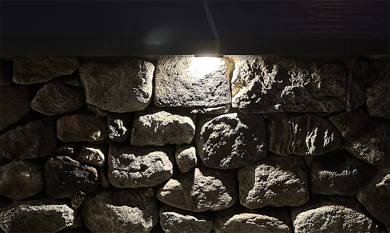 Landscape lighting illuminates a custom stone wall built by Nest Outdoors in Goffstown NH